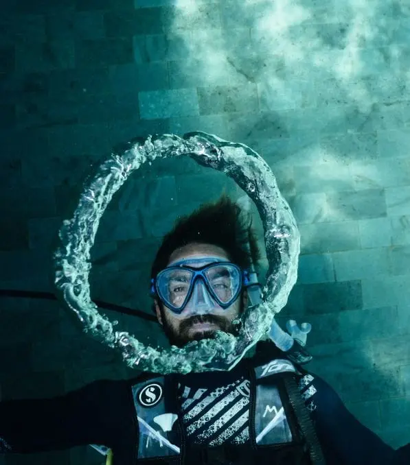Scuba diver in Nusa Penida underwater blowing a large circular air bubble ring around his masked face.