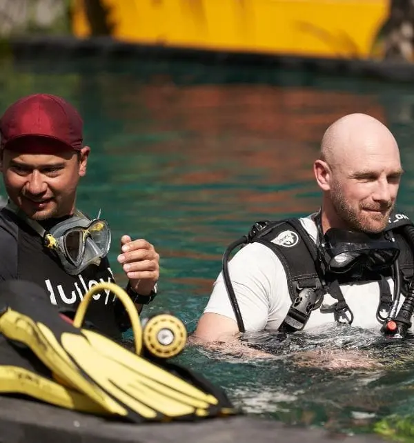 Two scuba divers preparing to dive in Nusa Penida waters, adjusting their gear with fins and a regulator nearby.